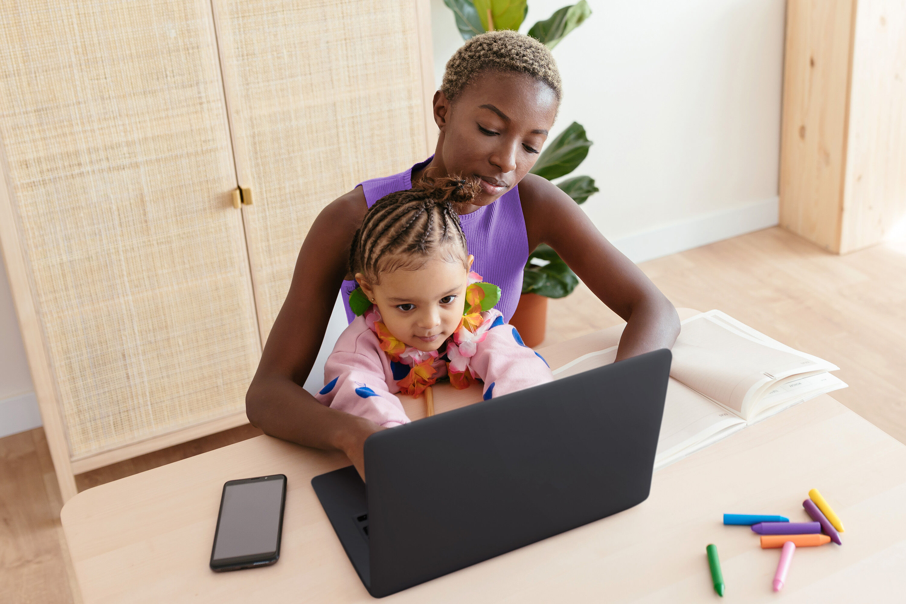 A daughter sitting on her mother's lap while she uses a laptop computer