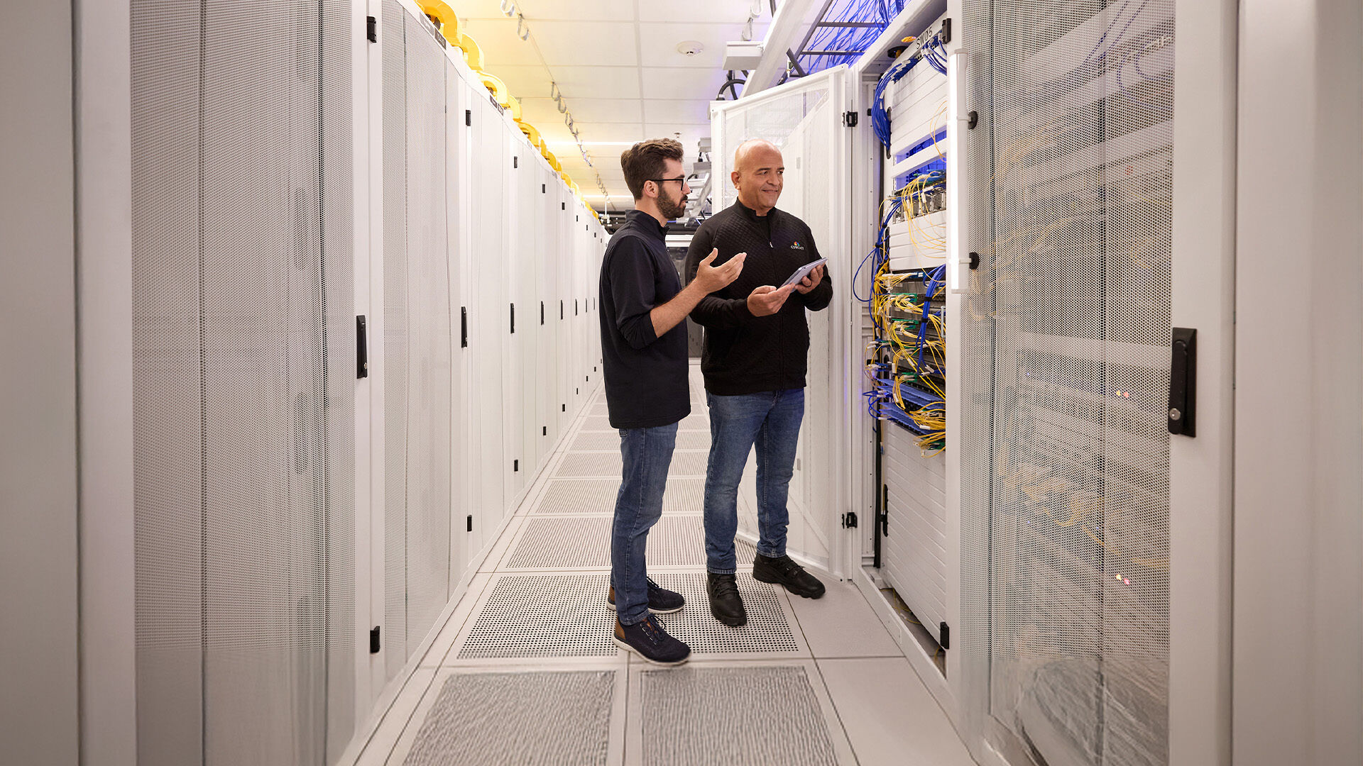 Technologists mid-conversation in a server room.