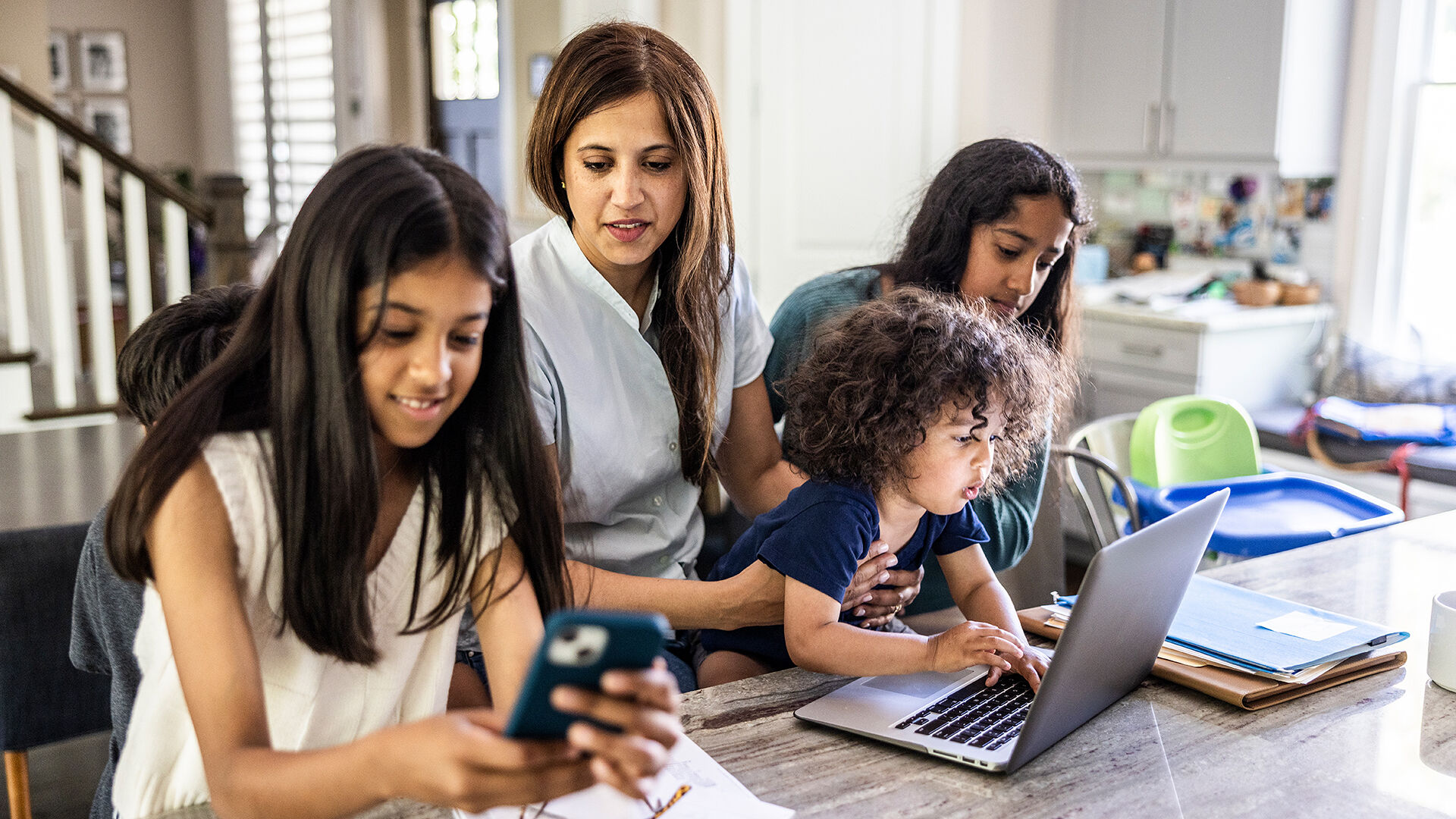 A family of four using a variety of devices while sitting at a kitchen table