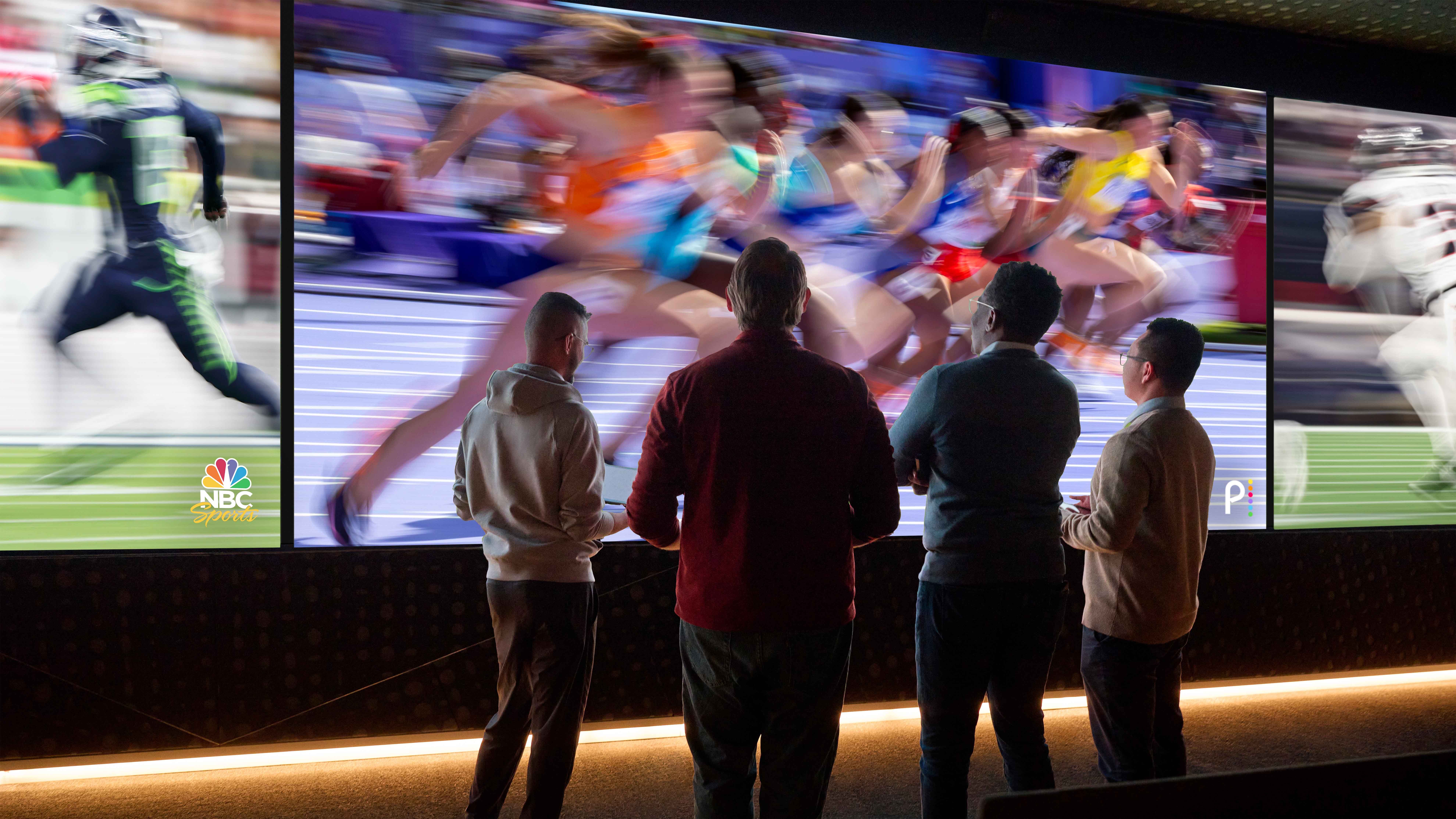 Four people silhouetted against a large screen displaying multiple sporting events