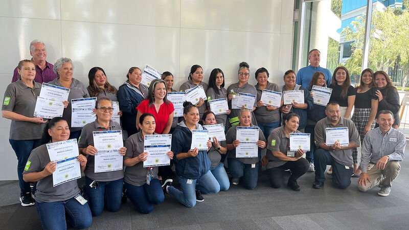 Large group of people holding up certificates together in a group photo outdoors