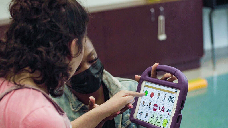 Two people sitting together while one guides the other in using an app on a tablet with a purple case