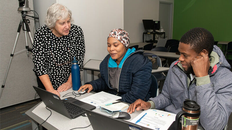 Instructor assisting two students as they review documents and work together at a desk with a laptop