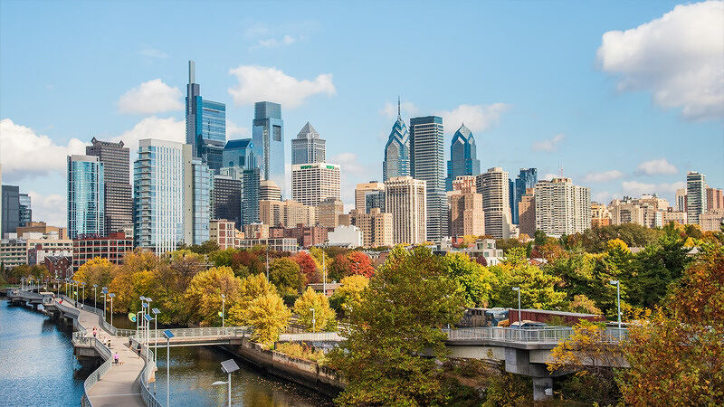 Skyline view of Philadelphia skyscrapers taken from across a river with autumn trees in the foreground