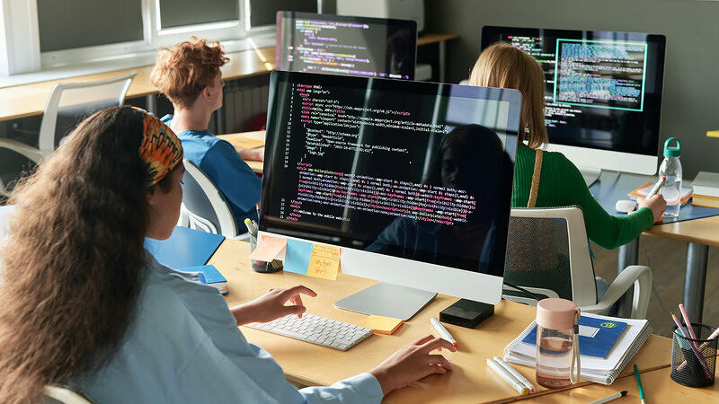 Person sitting at a desk with code displayed across a large computer screen in an office environment