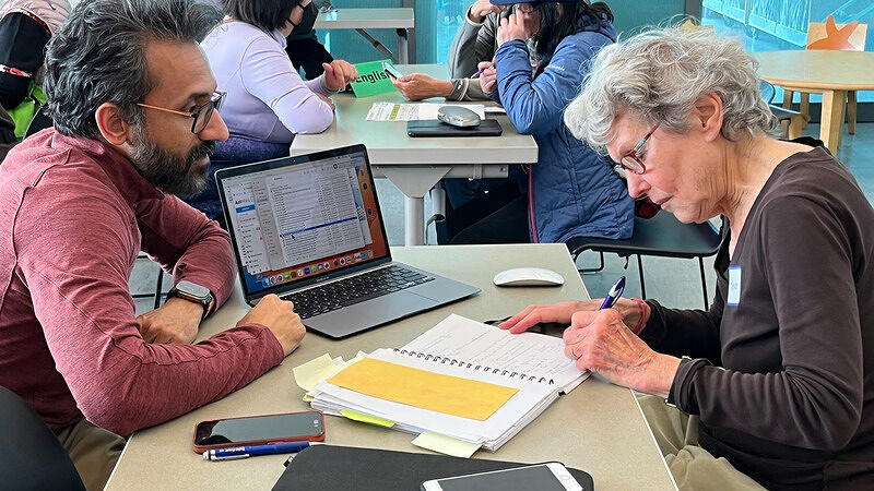 Man and woman sitting side-by-side at a desk reviewing notes and working on a laptop together