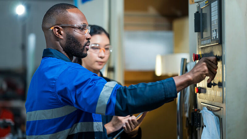 Technician in blue workwear adjusting control dials on industrial equipment alongside a colleague