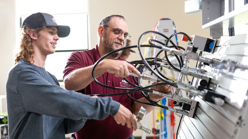 Two men working together to assemble or inspect complex wiring and machinery components