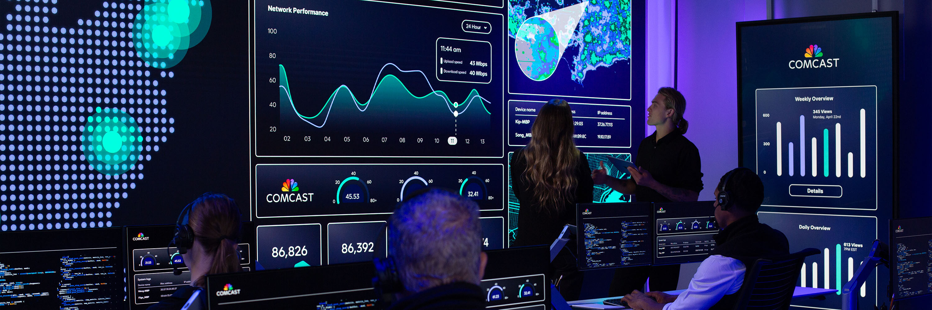 A modern operations center with multiple large screens displaying Comcast network performance dashboards while people sit at workstations and two colleagues stand discussing the data