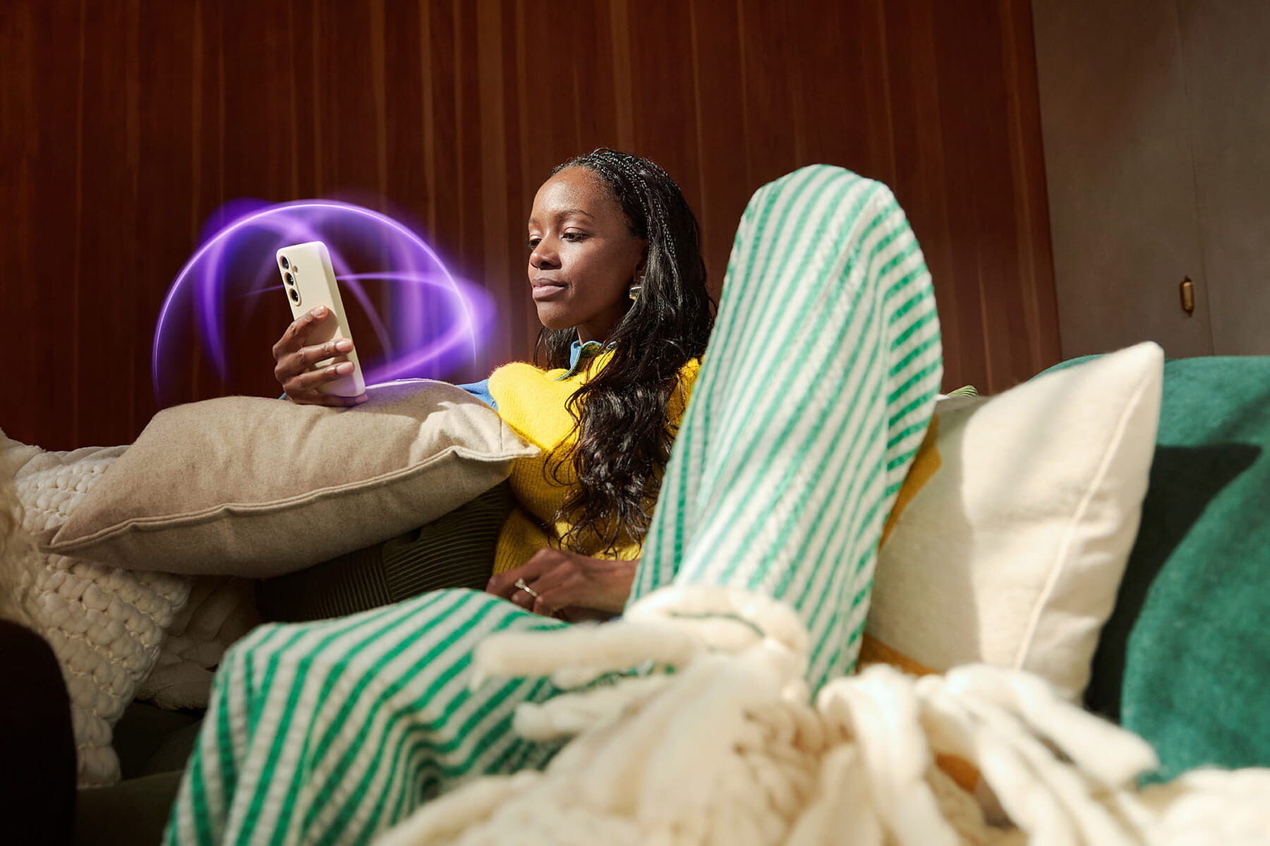 A woman relaxing on a couch, holding a smartphone as soft purple digital light effects glow around it