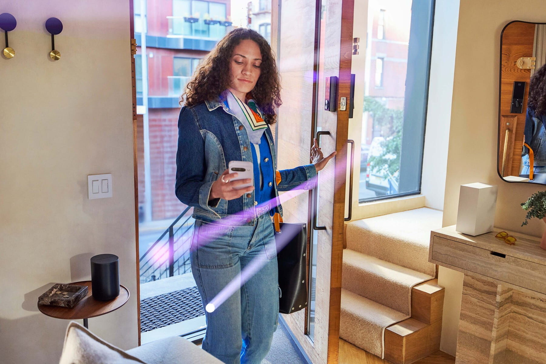 A person standing in a modern home entryway, looking at a smartphone as purple light beams suggest smart‑home activity