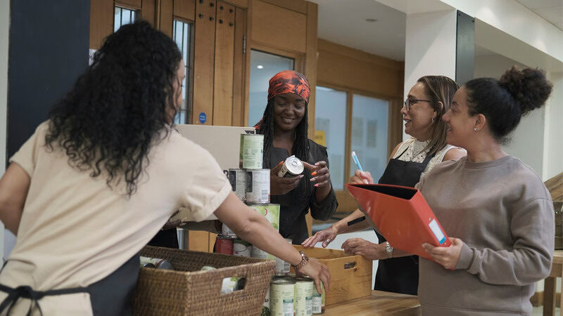 Four people sorting canned goods and supplies together at a food bank table in a brightly lit indoor room